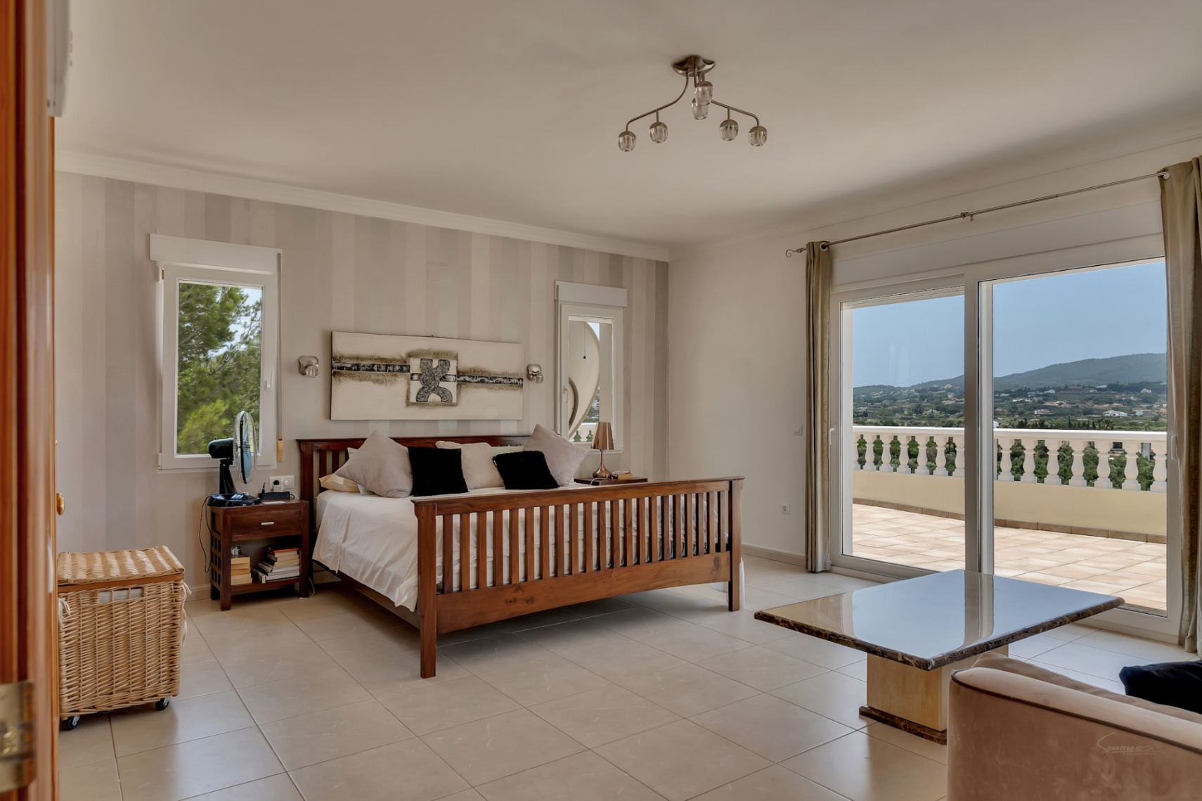 Dormitorio principal con cama de madera, pared de papel pintado a rayas y acceso directo a una amplia terraza con vistas panorámicas al valle y balustrada clásica.
