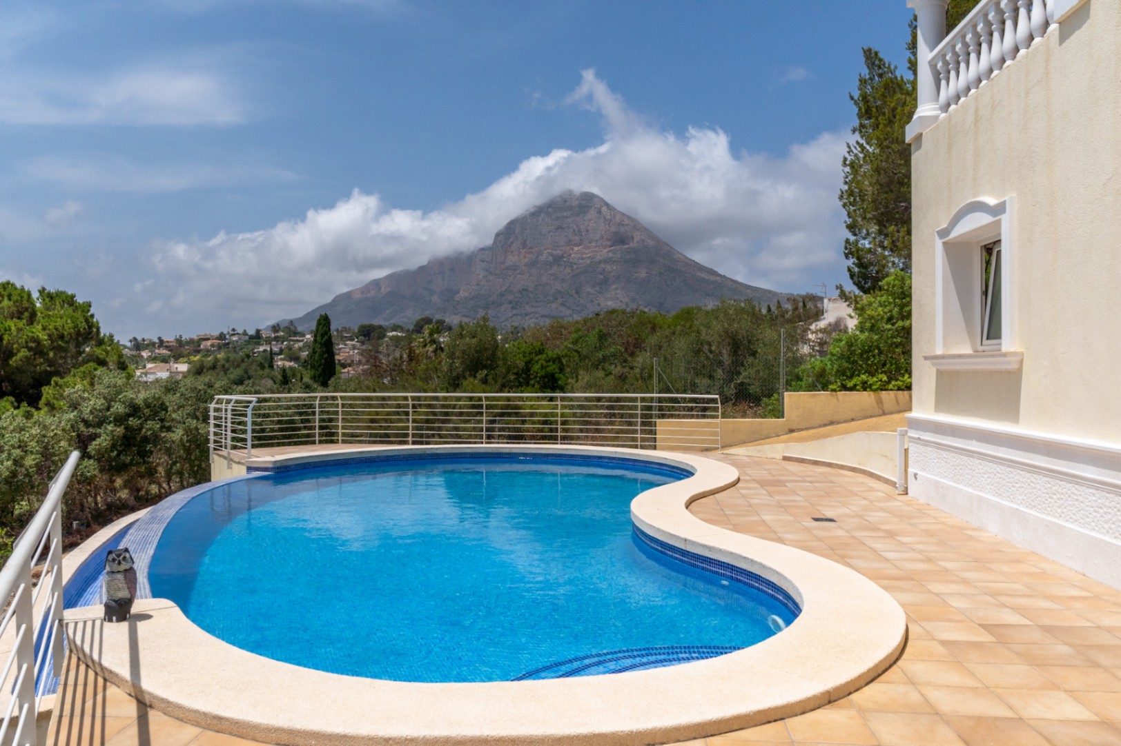 Piscina infinity de diseño curvo con vistas directas al macizo del Montgó, rodeada de una amplia terraza de gres y vegetación mediterránea.