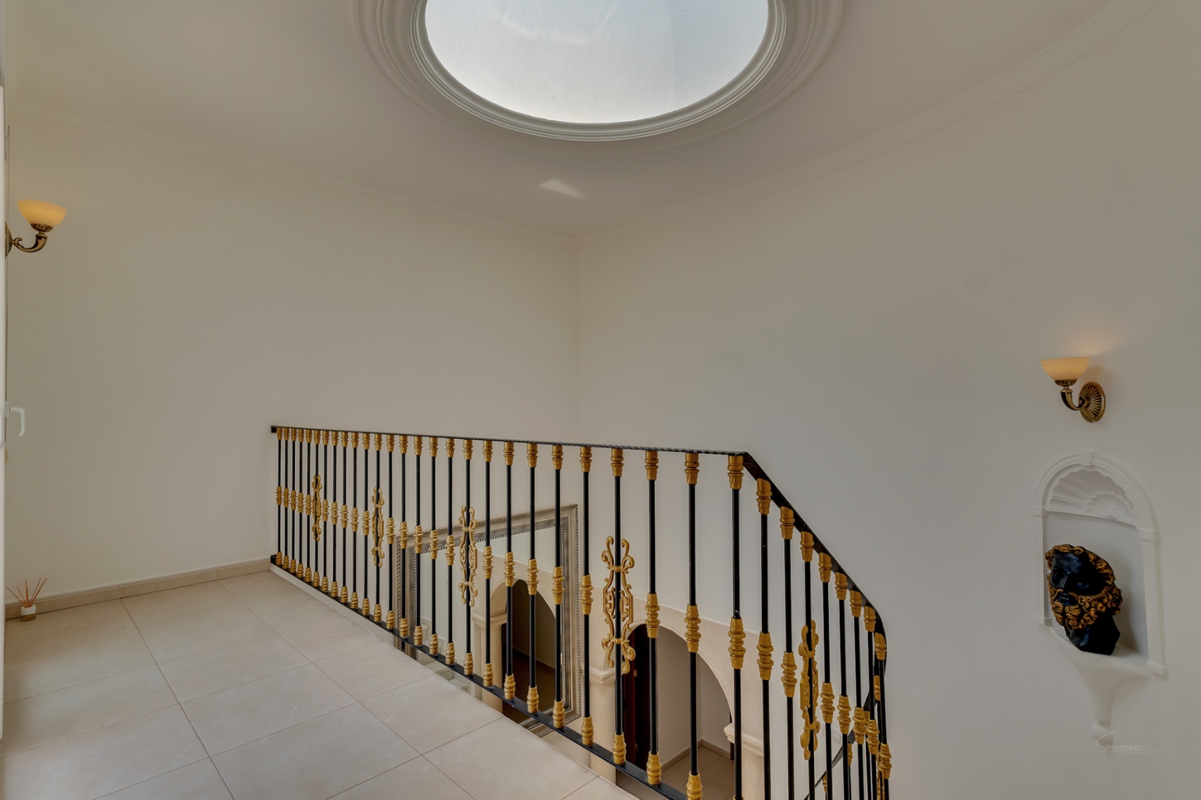 Rellano superior con cúpula acristalada circular, barandilla de hierro forjado con detalles dorados y hornacina decorativa en la pared.