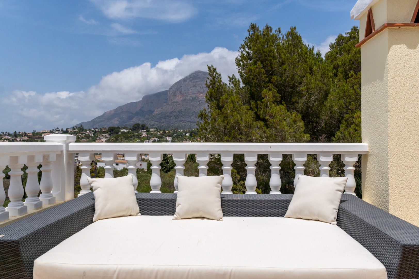 Terraza superior con cama de exterior en ratán y vistas despejadas al Montgó, delimitada por una balaustrada blanca clásica.