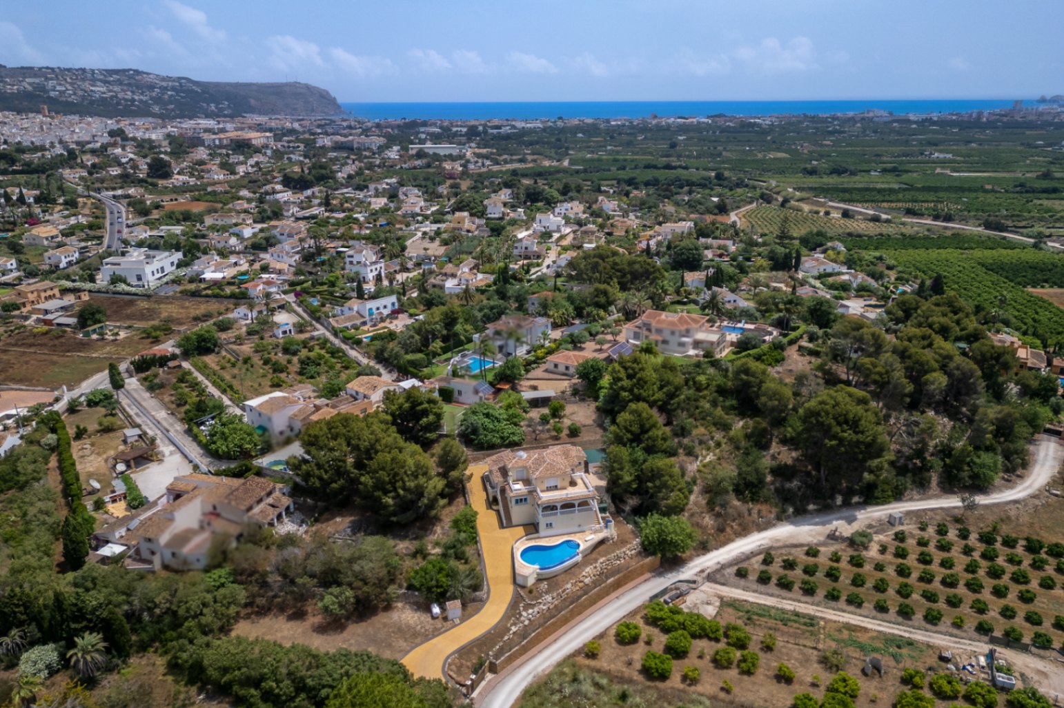Vista aérea de la propiedad elevada con piscina infinity curva, rodeada de pinos y campos, con vistas panorámicas que se extienden hasta el mar Mediterráneo.