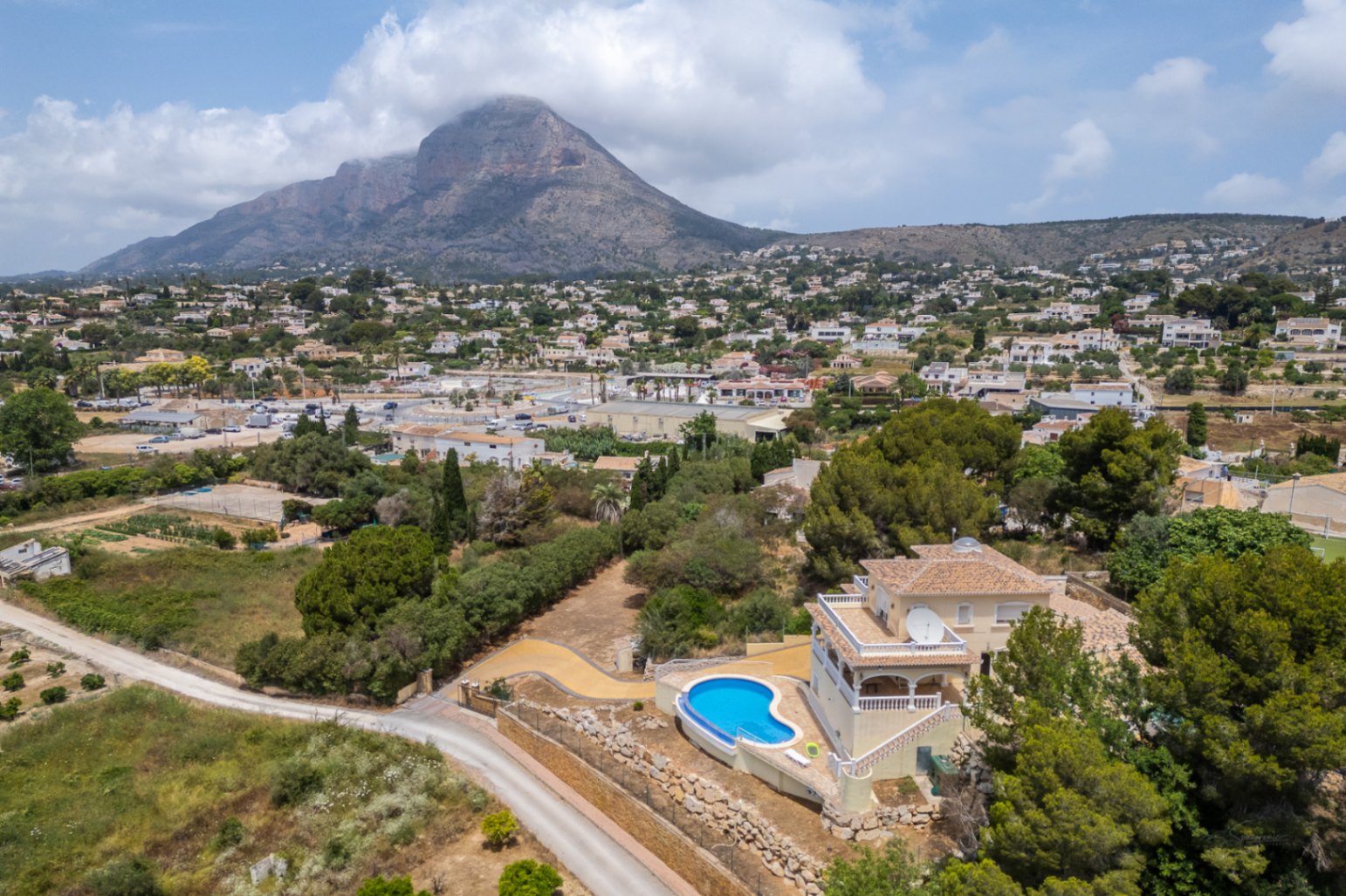 Vista aérea de la villa con piscina infinita de diseño curvo, destacando su posición elevada con vistas panorámicas al valle y al macizo del Montgó.