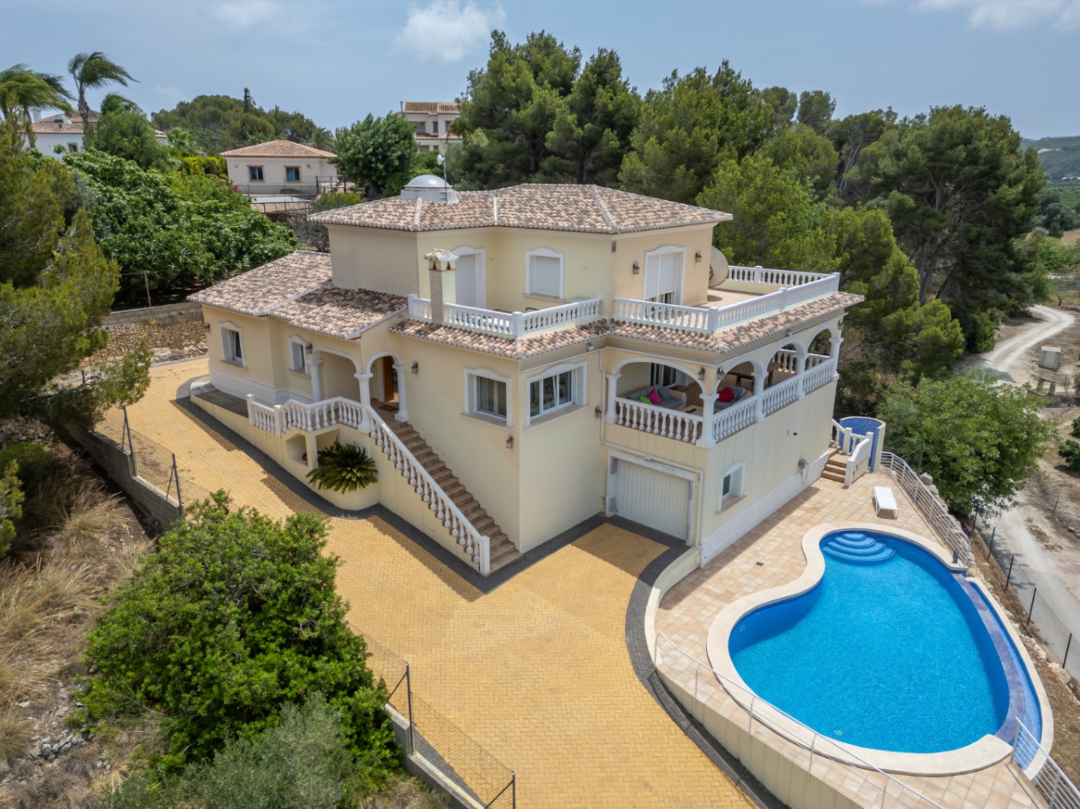 Vista aérea de la villa de estilo mediterráneo con piscina de forma orgánica, amplias terrazas con balaustradas blancas, naya arqueada y cúpula acristalada en el nivel superior.