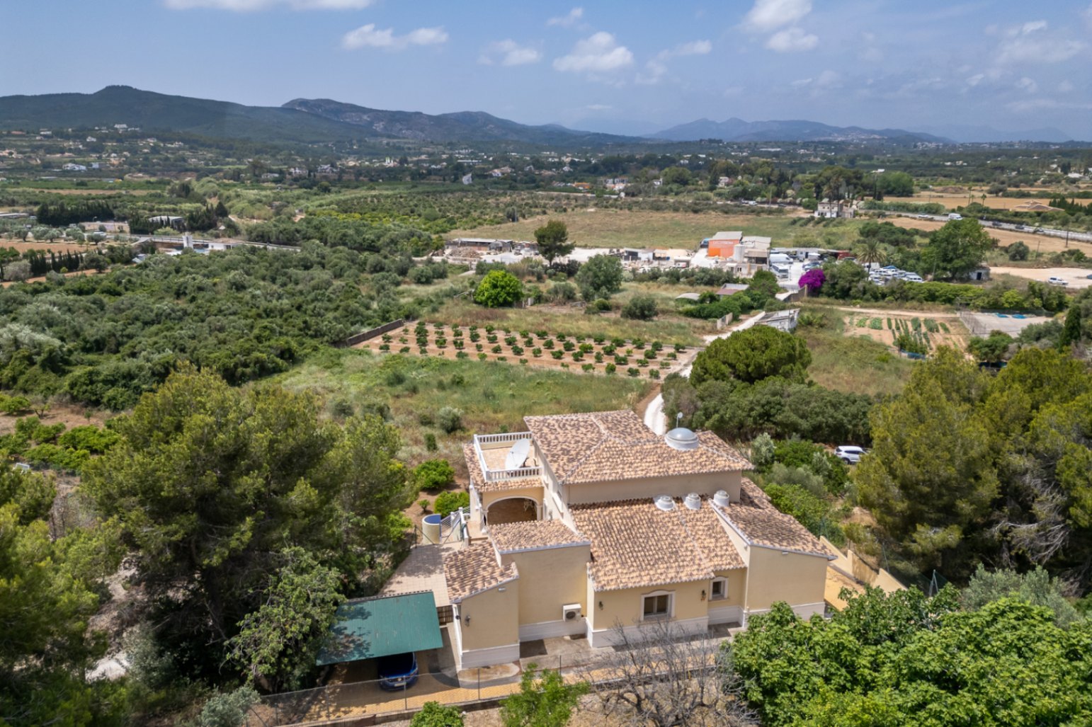 Vista aérea de la villa que muestra su tejado de teja árabe, la cúpula central acristalada y las claraboyas circulares, rodeada de campos y montañas.