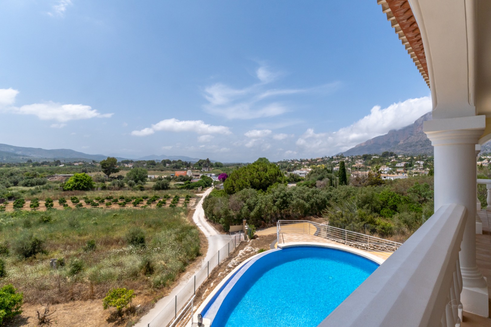 Vista desde la terraza superior que muestra la piscina infinity curva y vistas panorámicas de 180º sobre el valle de Jávea y el monte Montgó.