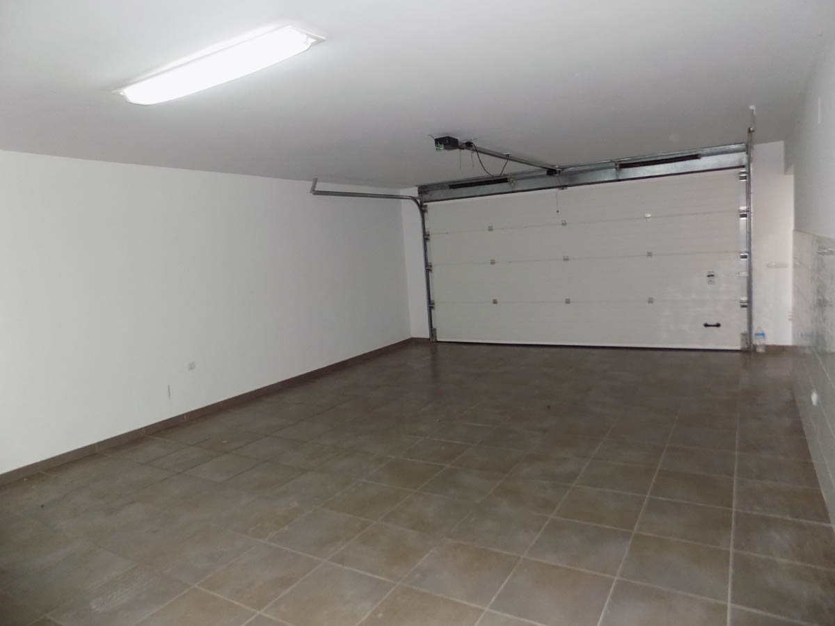Amplio garaje doble situado en la planta sótano, con suelo de gres cerámico, paredes blancas y puerta seccional automática de gran anchura.