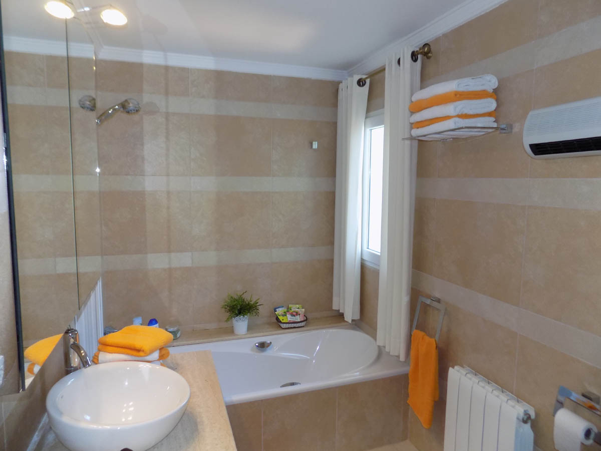 Baño equipado con bañera encastrada, lavabo de seno circular sobre encimera de piedra y paredes alicatadas en tonos crema y beige con bandas horizontales.