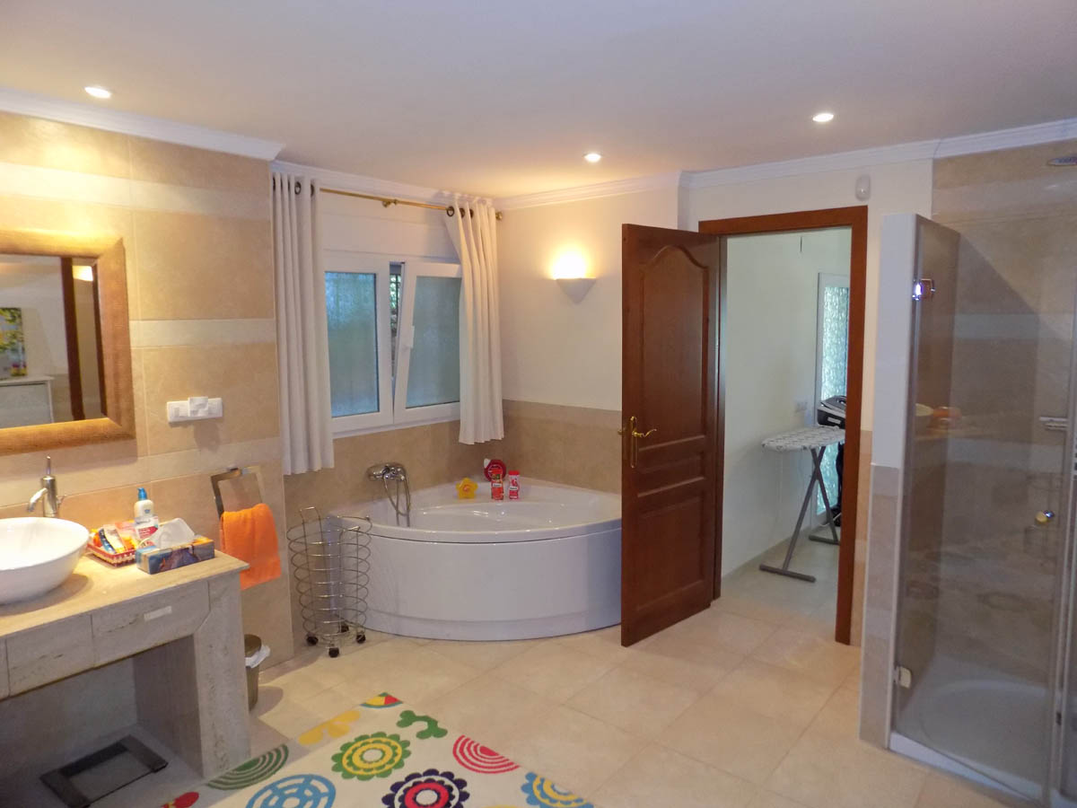 Cuarto de baño equipado con bañera de hidromasaje rinconera, ducha con mampara de cristal y encimera de piedra. Incluye iluminación empotrada y acceso a una zona de lavandería.