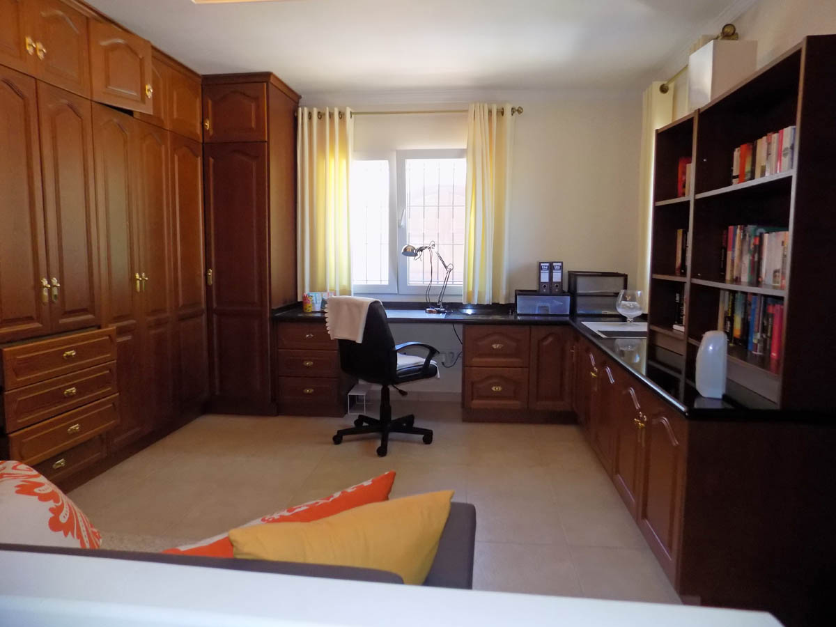 Despacho funcional con amplios armarios empotrados de madera, escritorio perimetral con encimera oscura y estantería integrada bajo luz natural.