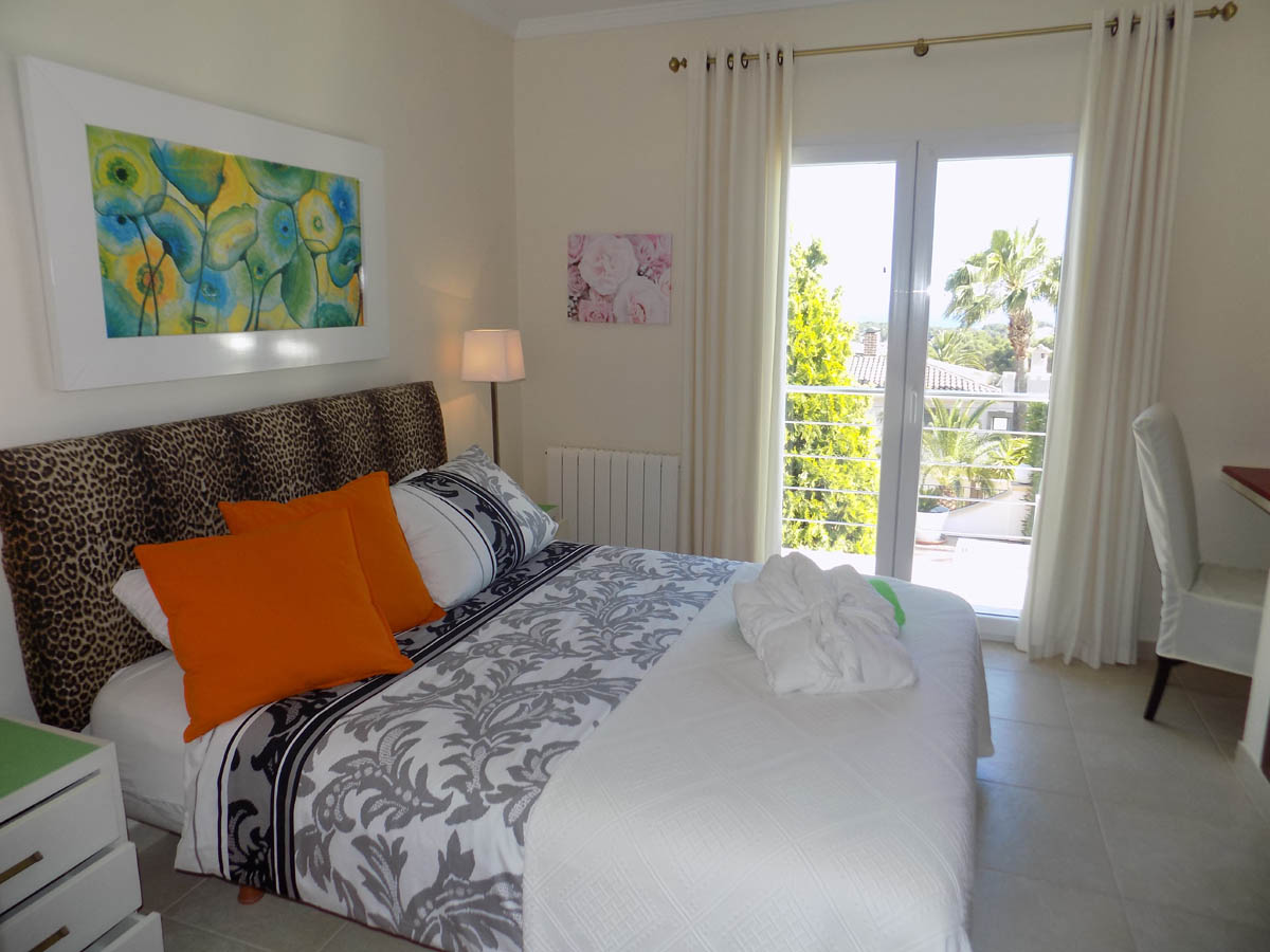 Dormitorio luminoso con acceso directo a la terraza, cama doble con cabecero de leopardo y vistas al jardín mediterráneo a través de grandes ventanales.