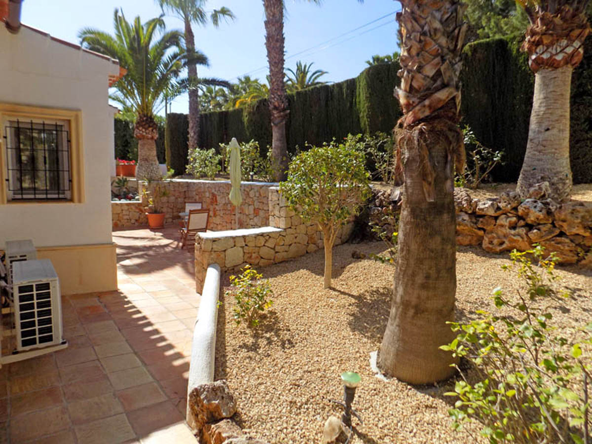 Jardín mediterráneo con muros de piedra seca, palmeras maduras y suelos de terracota. El paisajismo incluye zonas de grava y setos altos para mayor privacidad.