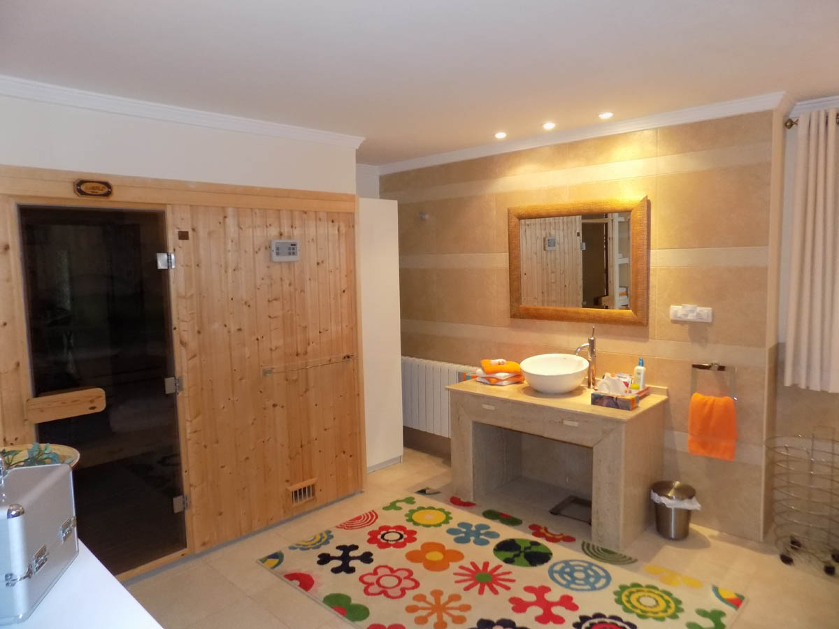 Zona de bienestar con sauna de madera integrada, lavabo sobre encimera de piedra y paredes alicatadas en tonos cálidos con iluminación empotrada.