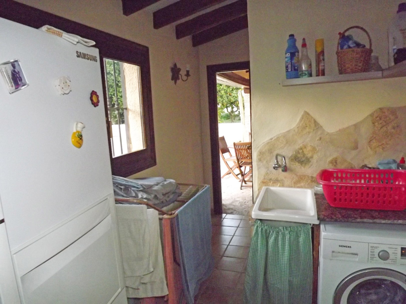 Cuarto de lavado funcional con vigas de madera, lavadora Siemens, fregadero con detalle de piedra y acceso directo a la terraza exterior.
