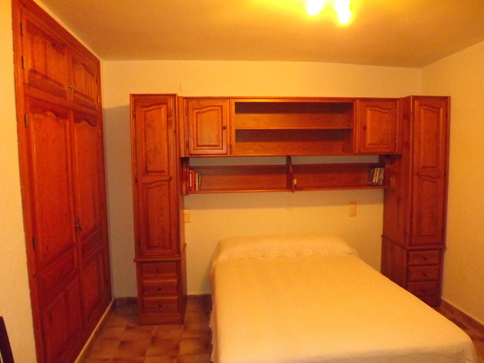 Dormitorio con mobiliario de madera maciza, incluyendo un armario empotrado y un puente sobre la cama con estanterías y almacenaje integrado.