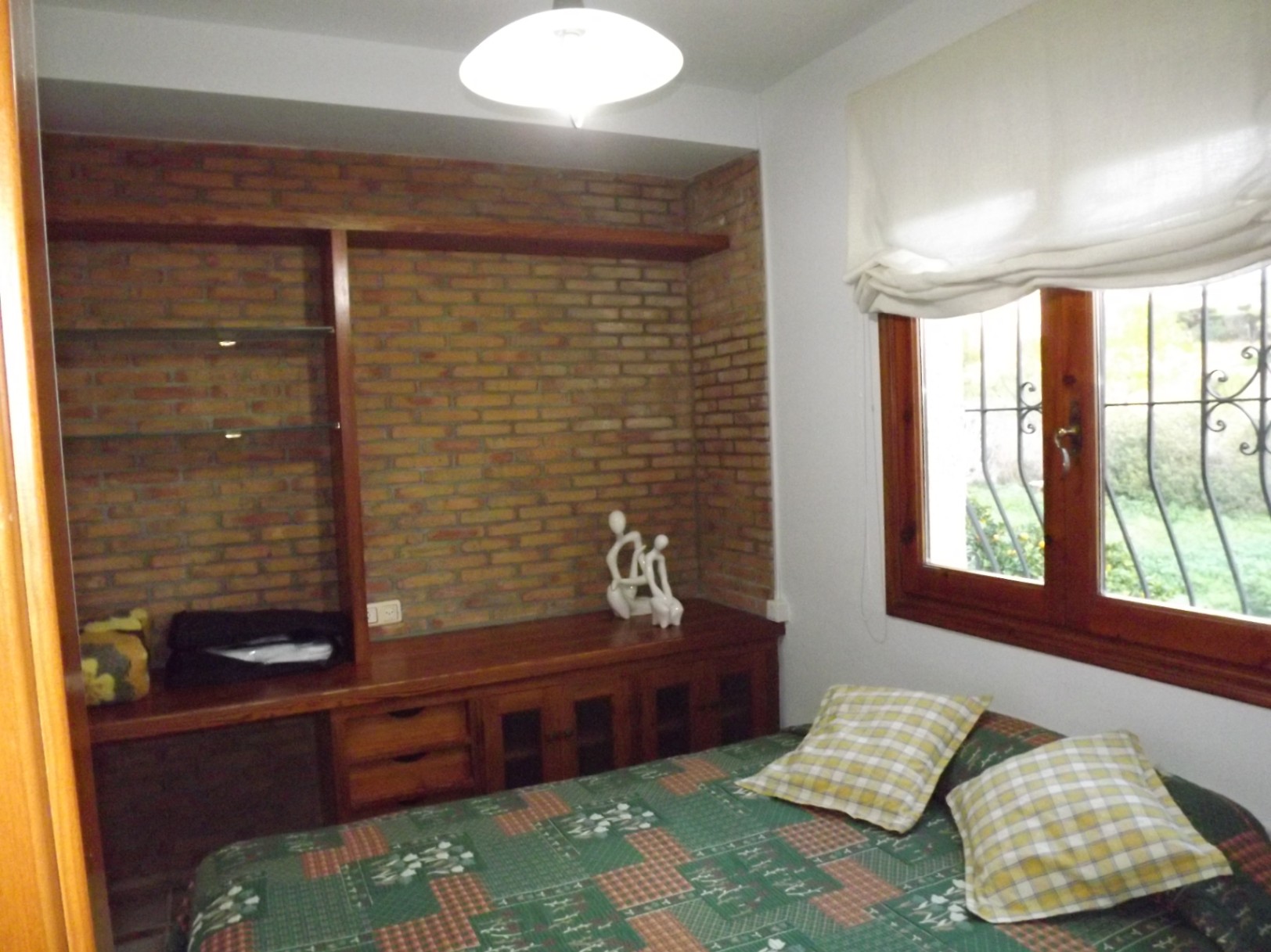 Dormitorio con pared de ladrillo visto, mobiliario de madera integrado con estanterías de cristal y ventana de madera con vistas al exterior.