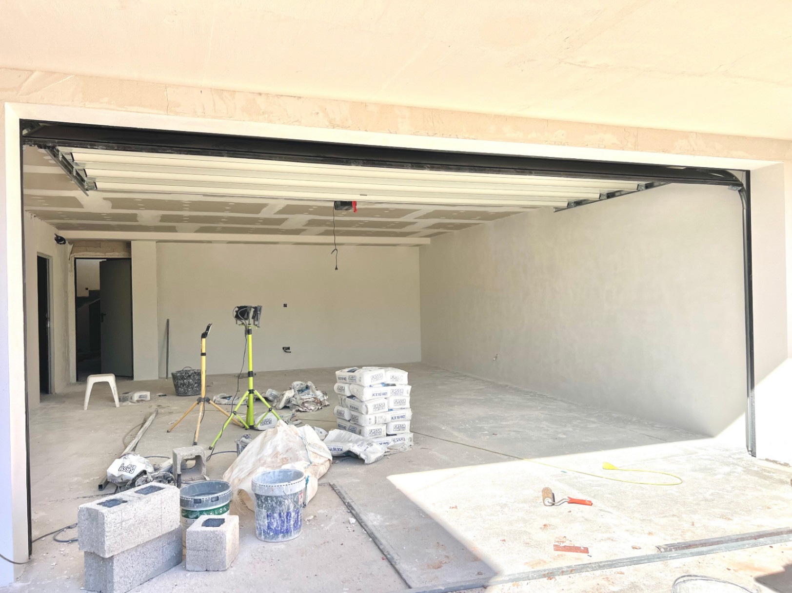Amplio garaje en fase de construcción con puerta seccional blanca, techos altos y espacio diáfano para varios vehículos o usos adicionales.