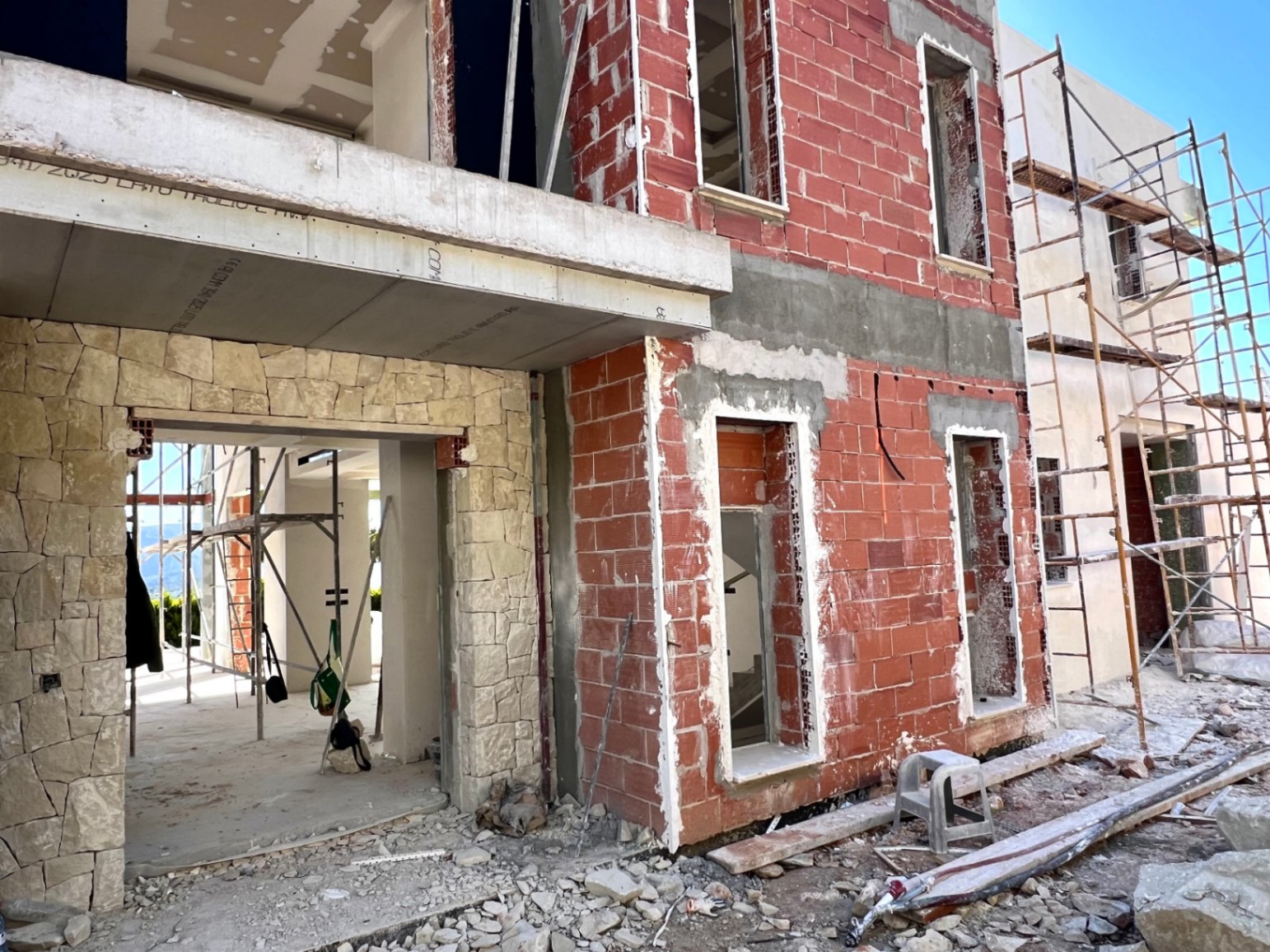 Estado actual de la construcción mostrando la fachada de ladrillo cerámico, revestimiento de piedra natural y estructura de hormigón con andamiaje exterior.