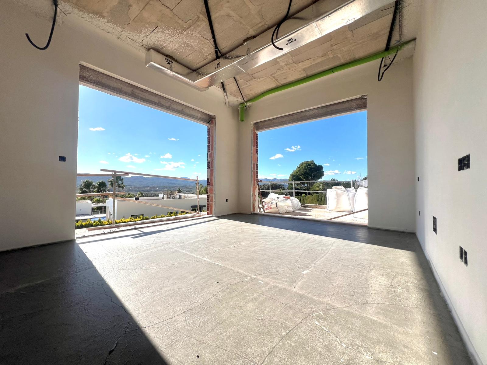 Interior en construcción con amplios ventanales que ofrecen vistas despejadas al valle, destacando los techos de hormigón y conductos de climatización.