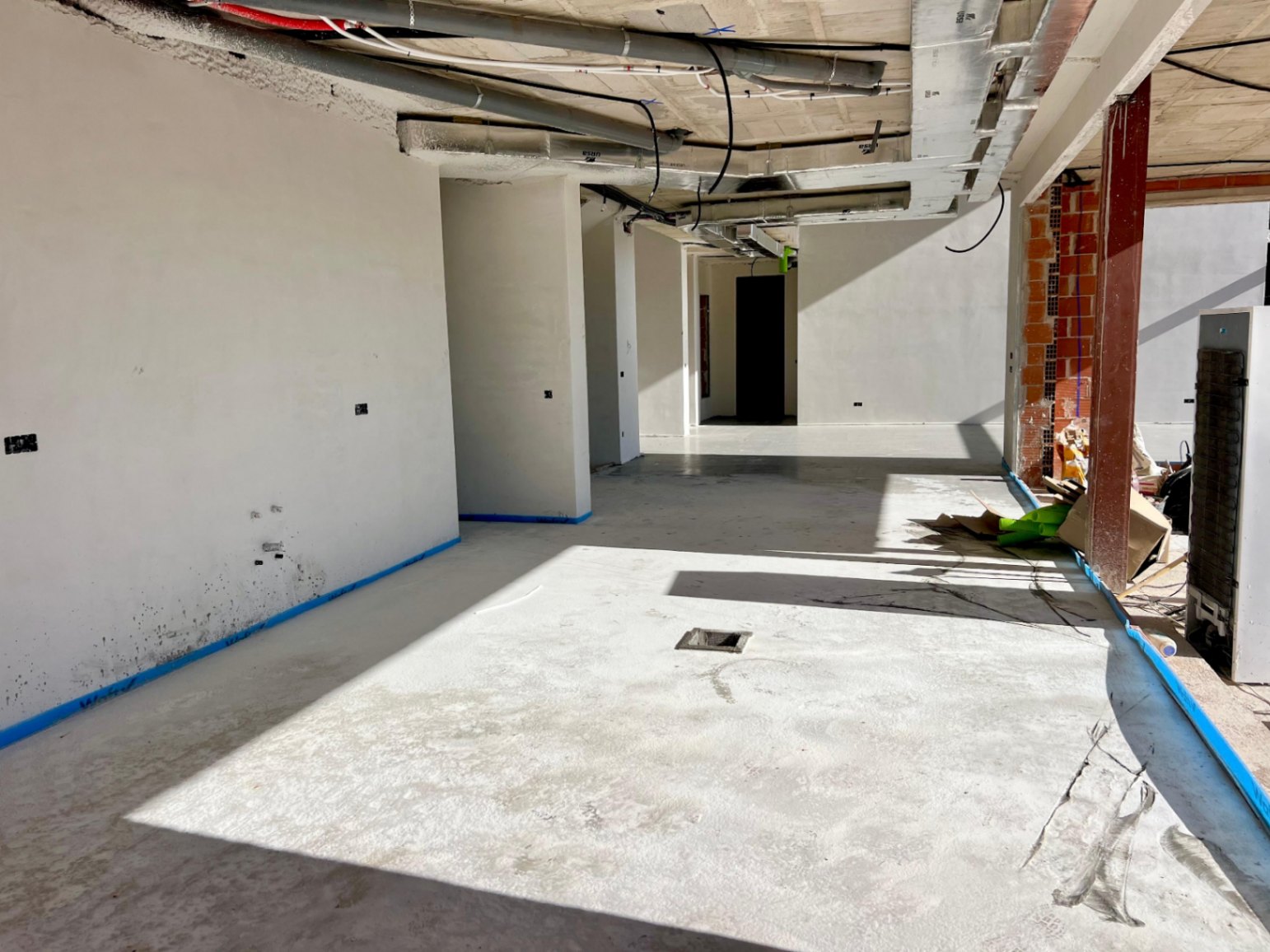 Vista del interior en fase de construcción con muros enlucidos, instalaciones de techo expuestas y una distribución diáfana que maximiza la entrada de luz natural.