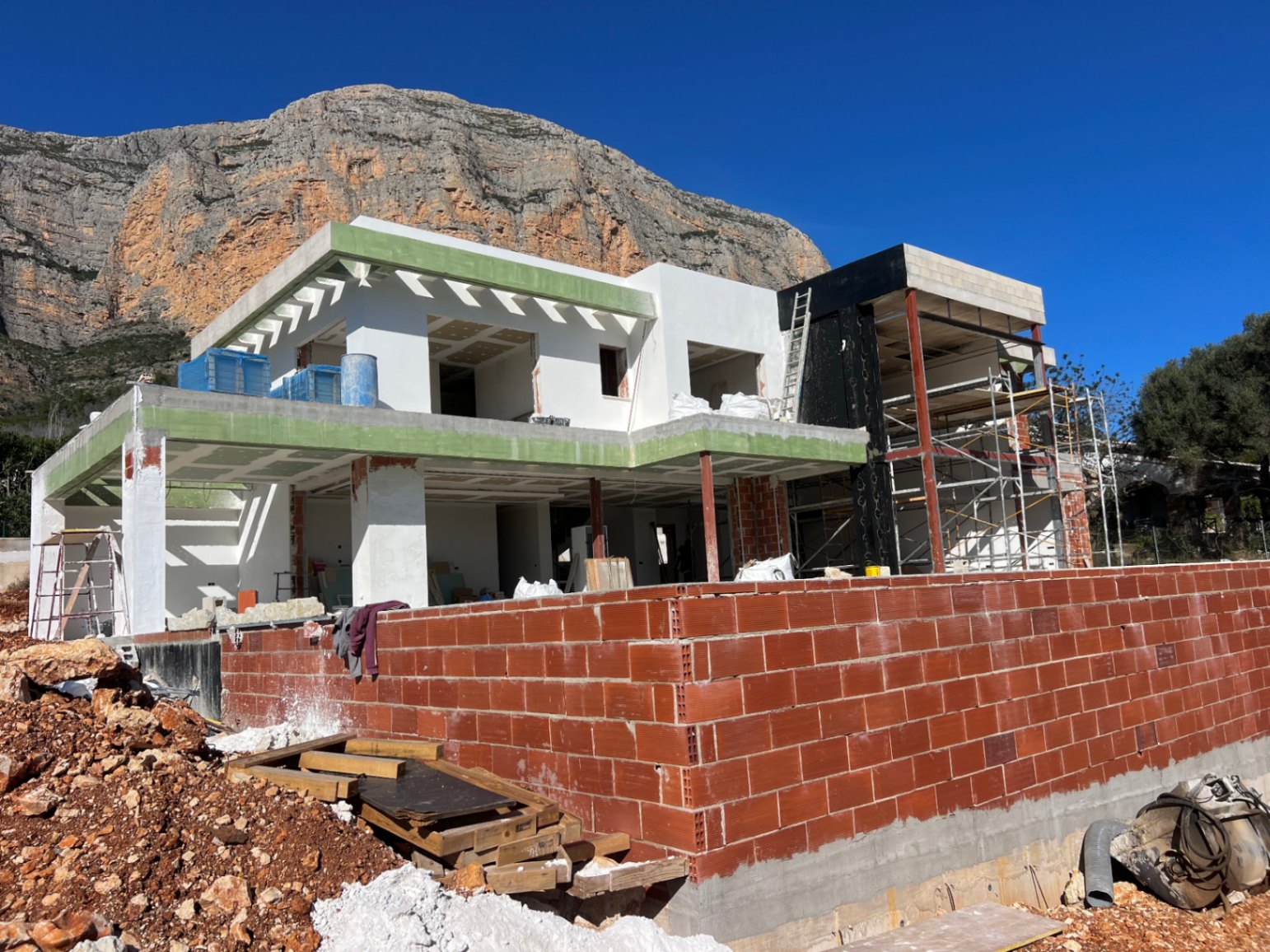 Vista exterior de la estructura en construcción de la villa moderna, destacando los amplios ventanales y la imponente silueta del Montgó al fondo.