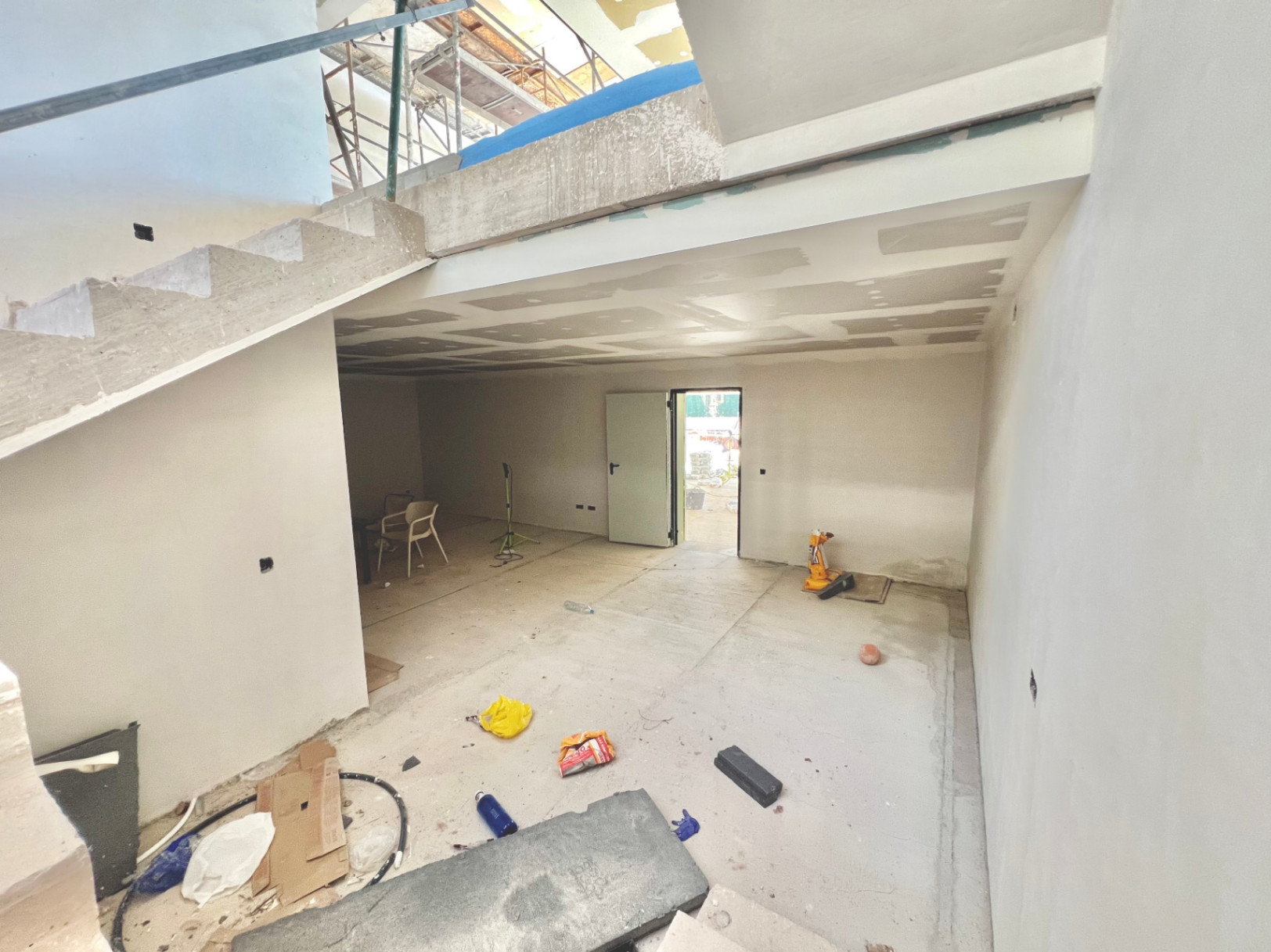 Vista interior de la planta inferior en construcción, mostrando la estructura de la escalera de hormigón y el espacio diáfano para gimnasio o cine.