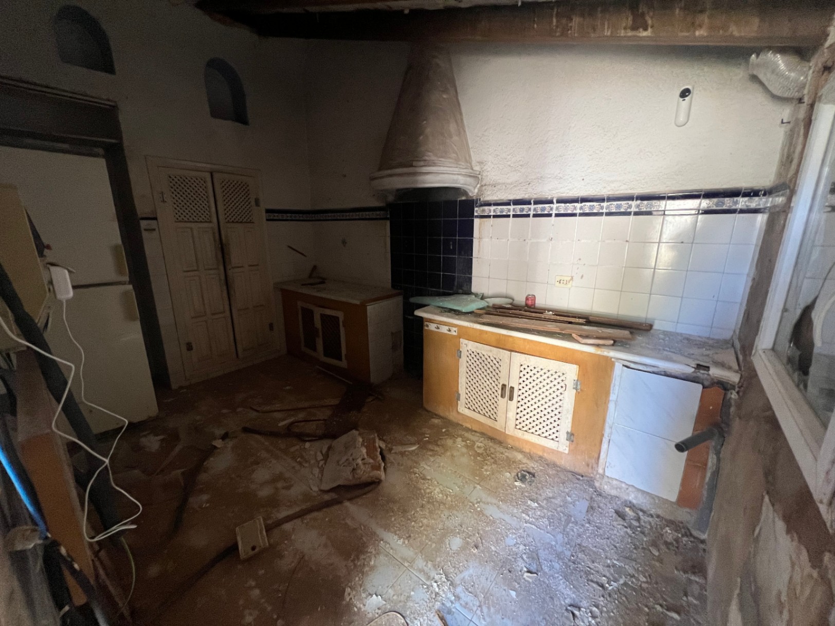 Cocina rústica para reformar con campana de obra cónica, azulejos tradicionales en blanco y azul, muebles de madera con celosía y nichos decorativos en la pared.