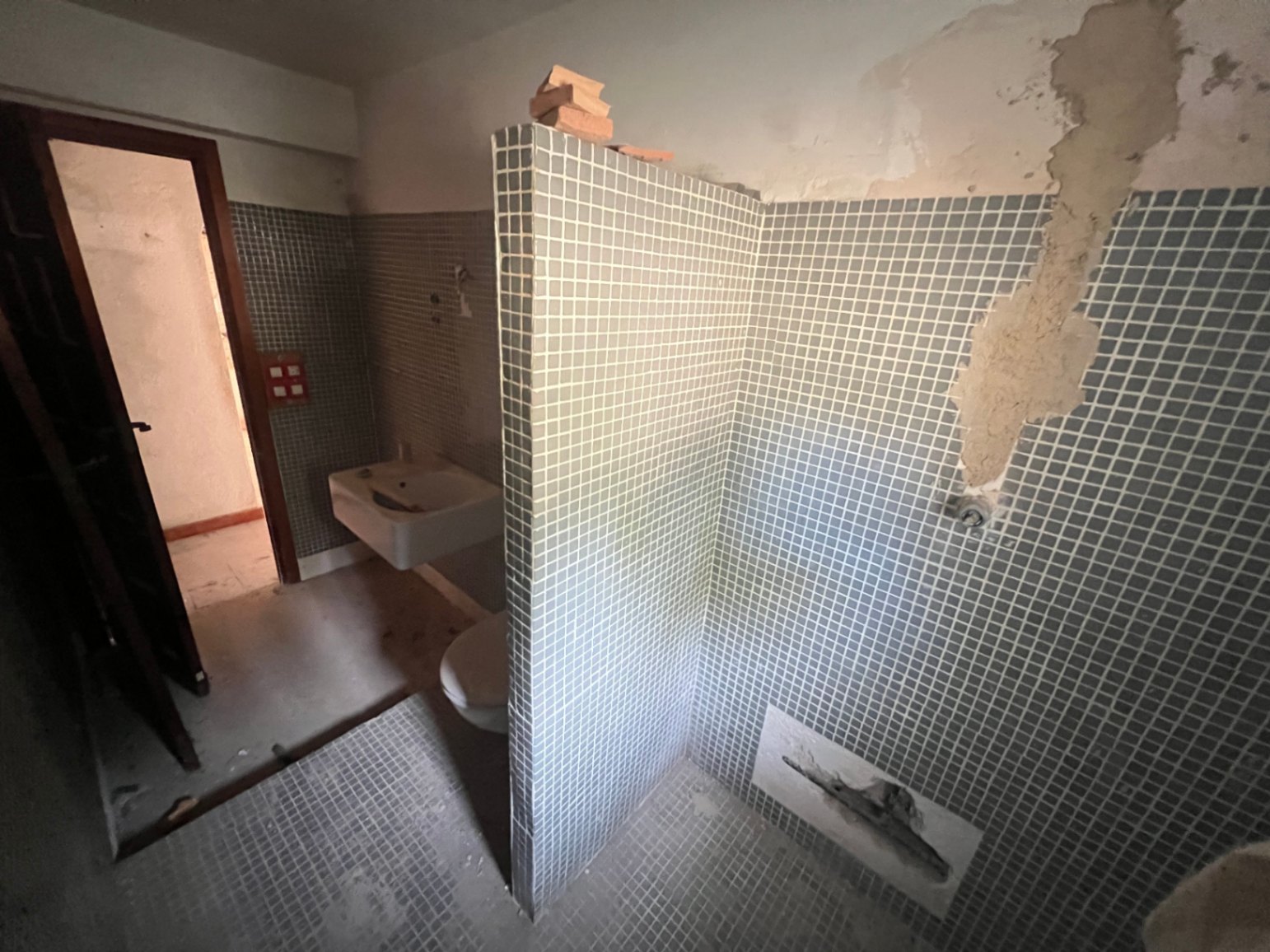 Cuarto de baño para reformar con azulejos tipo gresite azul, zona de ducha tabicada y sanitarios originales, ofreciendo un lienzo en blanco para un diseño moderno.