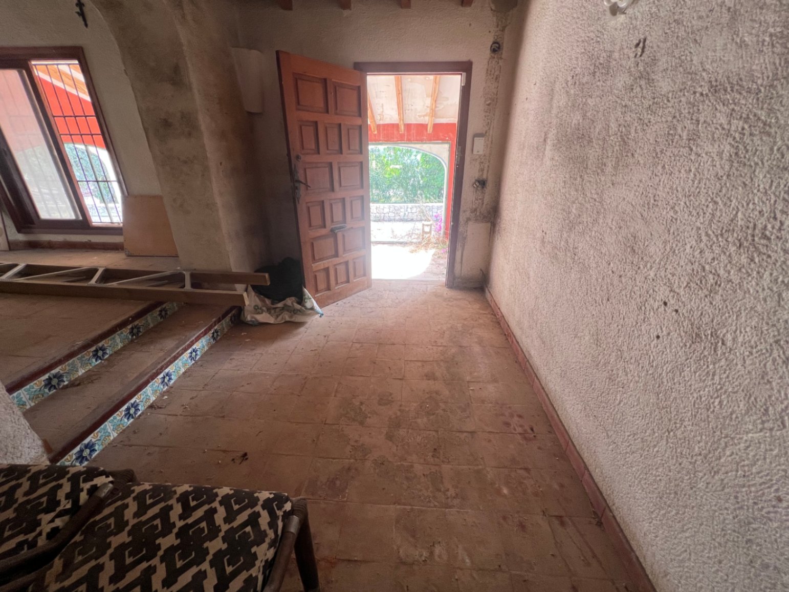 Entrada principal con suelos de barro, puerta de madera cuarteronada y escalones decorados con azulejos tradicionales, lista para una reforma integral.