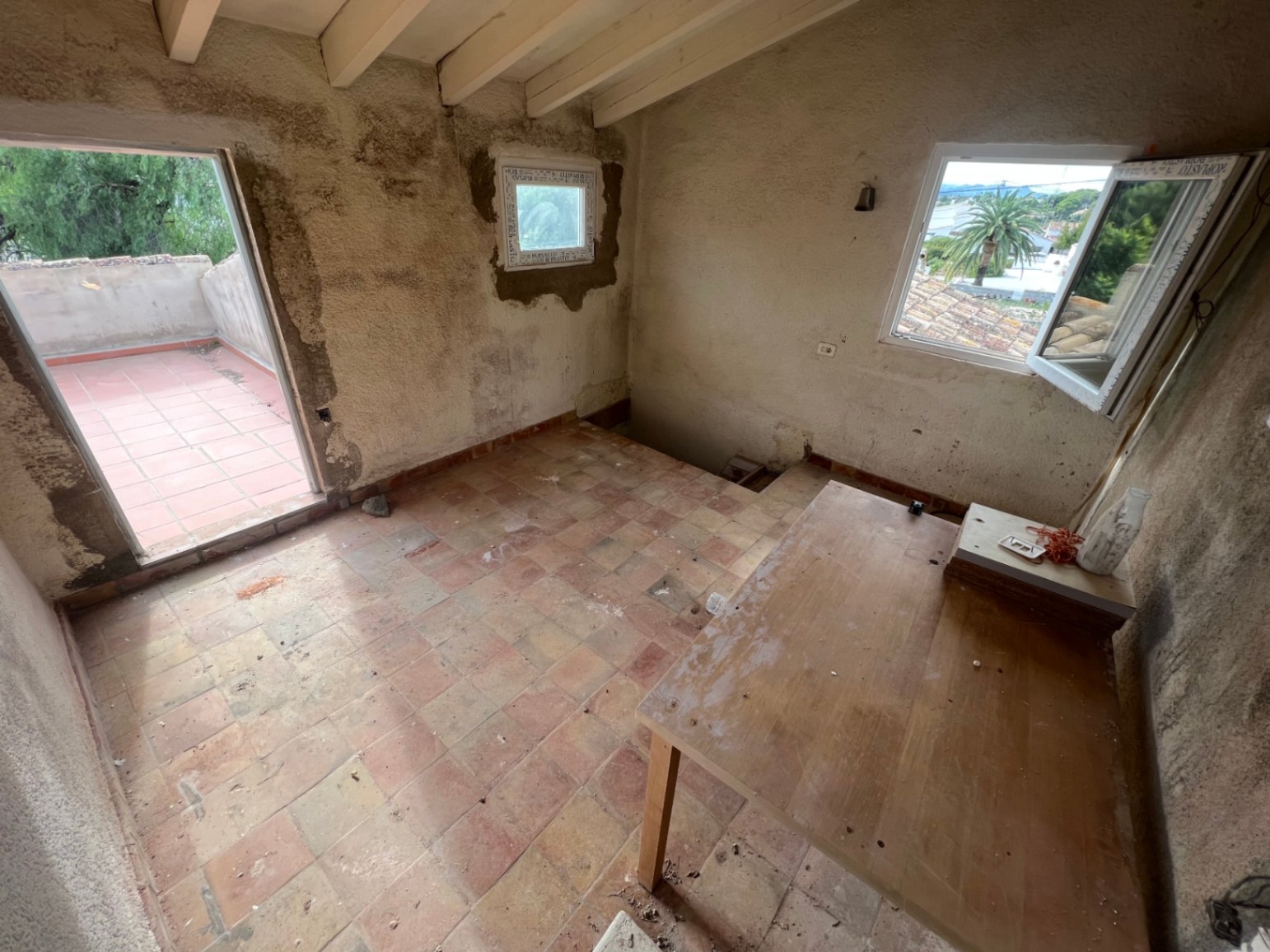 Habitación en planta superior para reformar con vigas de madera, suelos de terracota y acceso directo a una terraza privada con vistas despejadas.