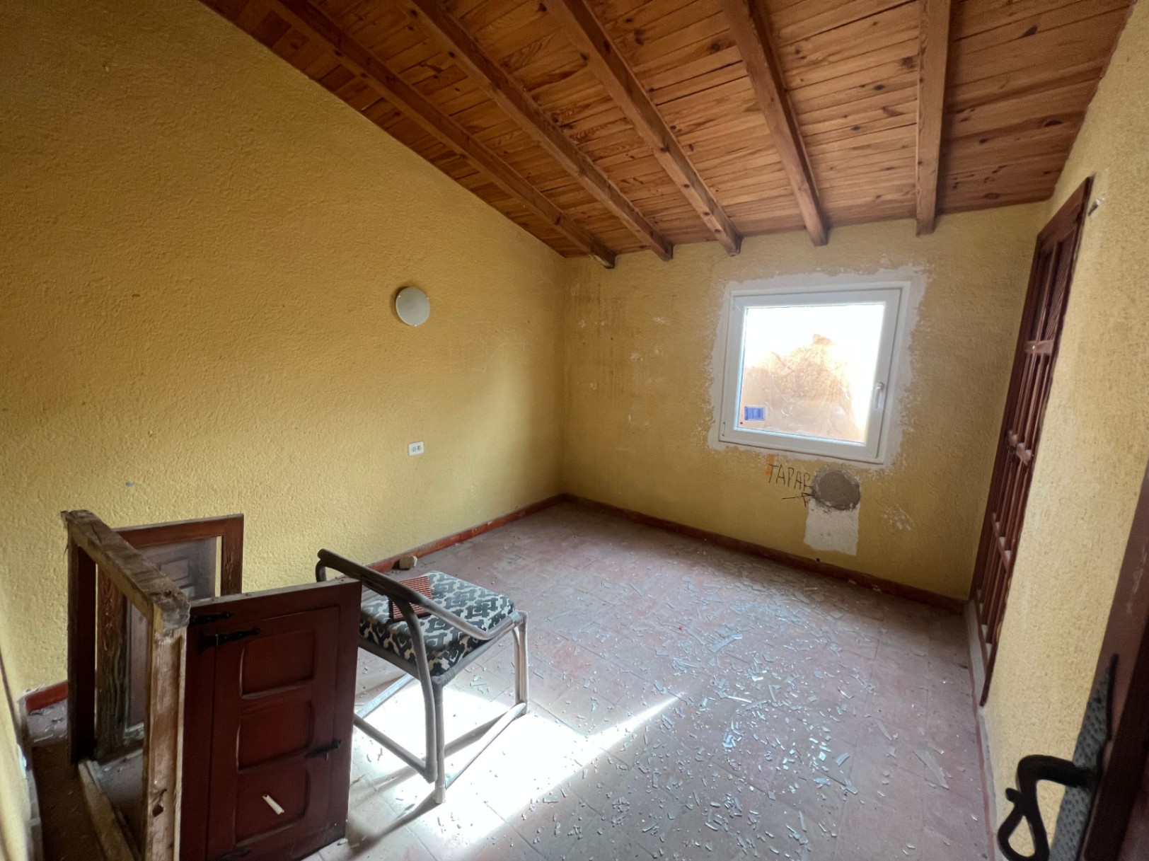 Habitación interior con techos de vigas de madera inclinadas, suelos de terracota y paredes amarillas. El espacio requiere reforma integral y cuenta con luz natural.