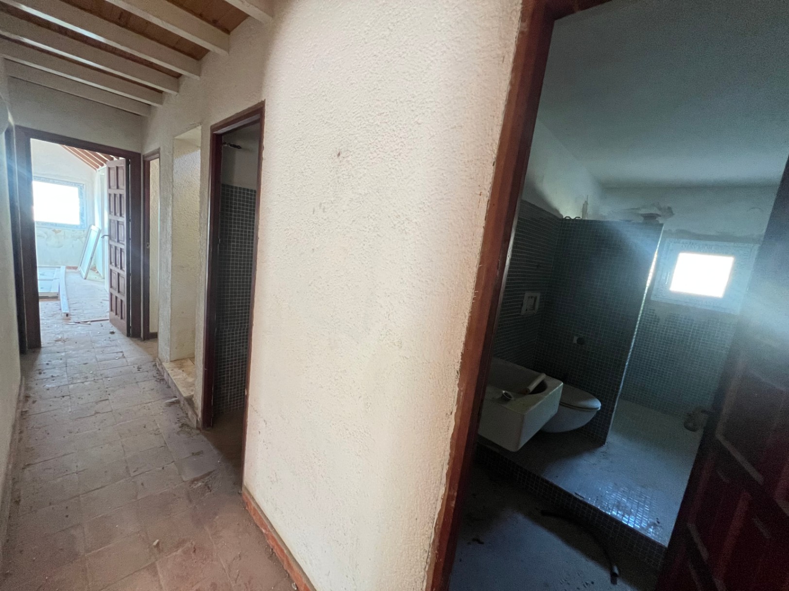 Pasillo interior con techos de vigas de madera y acceso a un baño con azulejos de mosaico azul. La estancia muestra el potencial de reforma integral de la vivienda.