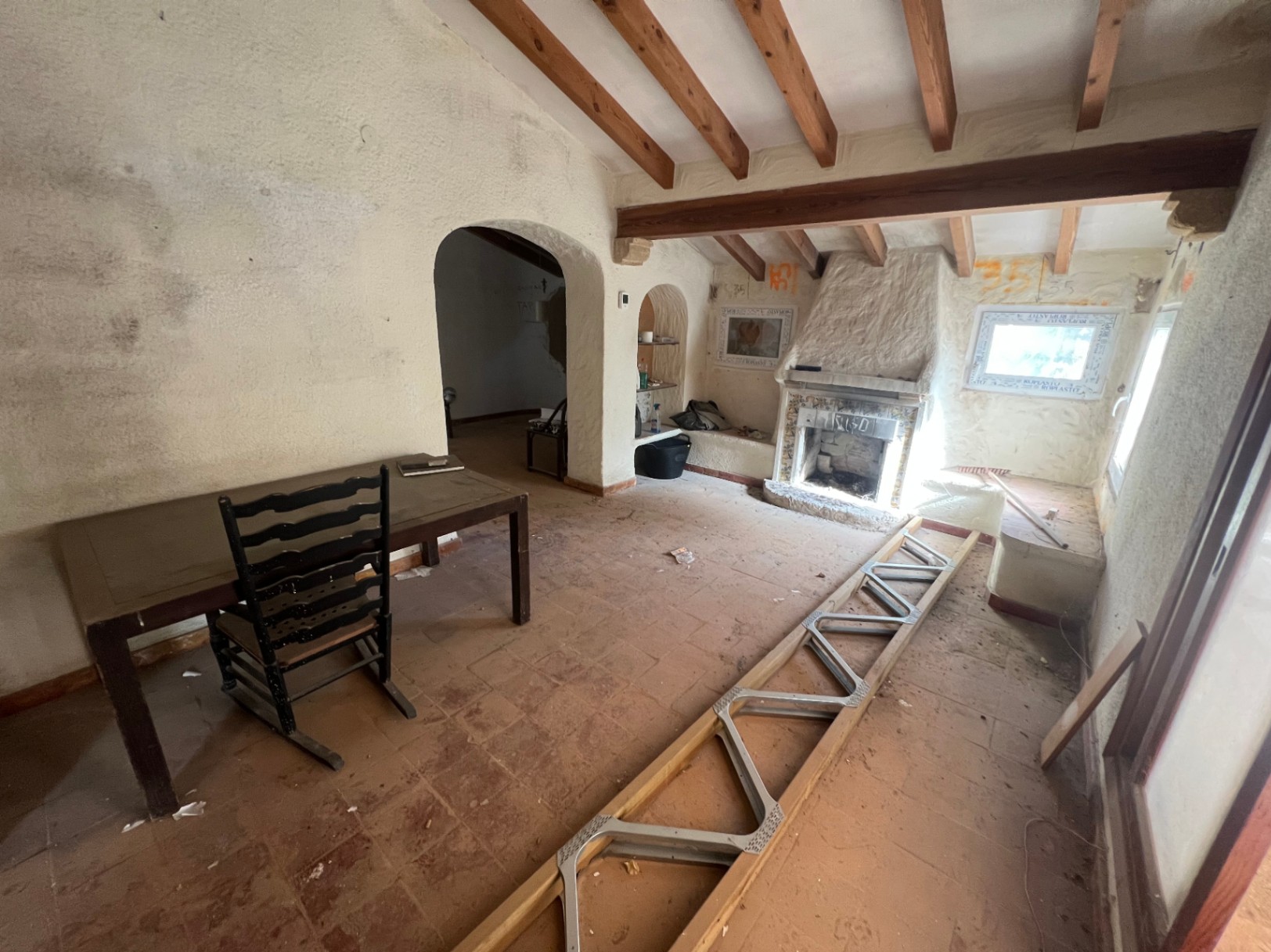 Salón rústico con vigas de madera a la vista, suelos de terracota y una chimenea de obra. El espacio cuenta con techos inclinados y arcos que conectan con otras estancias.