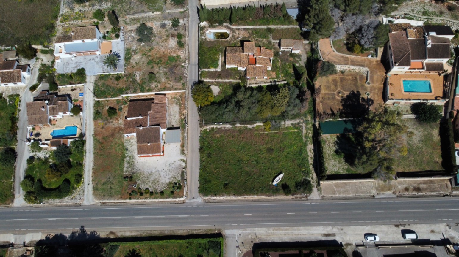 Vista aérea de la parcela de 2.895m2 en Jávea, destacando la vivienda existente, el amplio terreno disponible para ampliar y el acceso desde la vía principal.