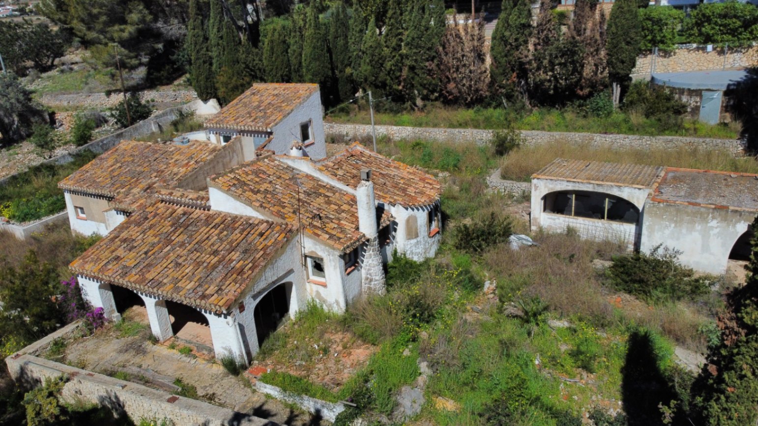 Vista aérea de la propiedad que muestra la arquitectura tradicional con tejados de teja cerámica, naya con arcos y una parcela extensa rodeada de vegetación y muros de piedra.