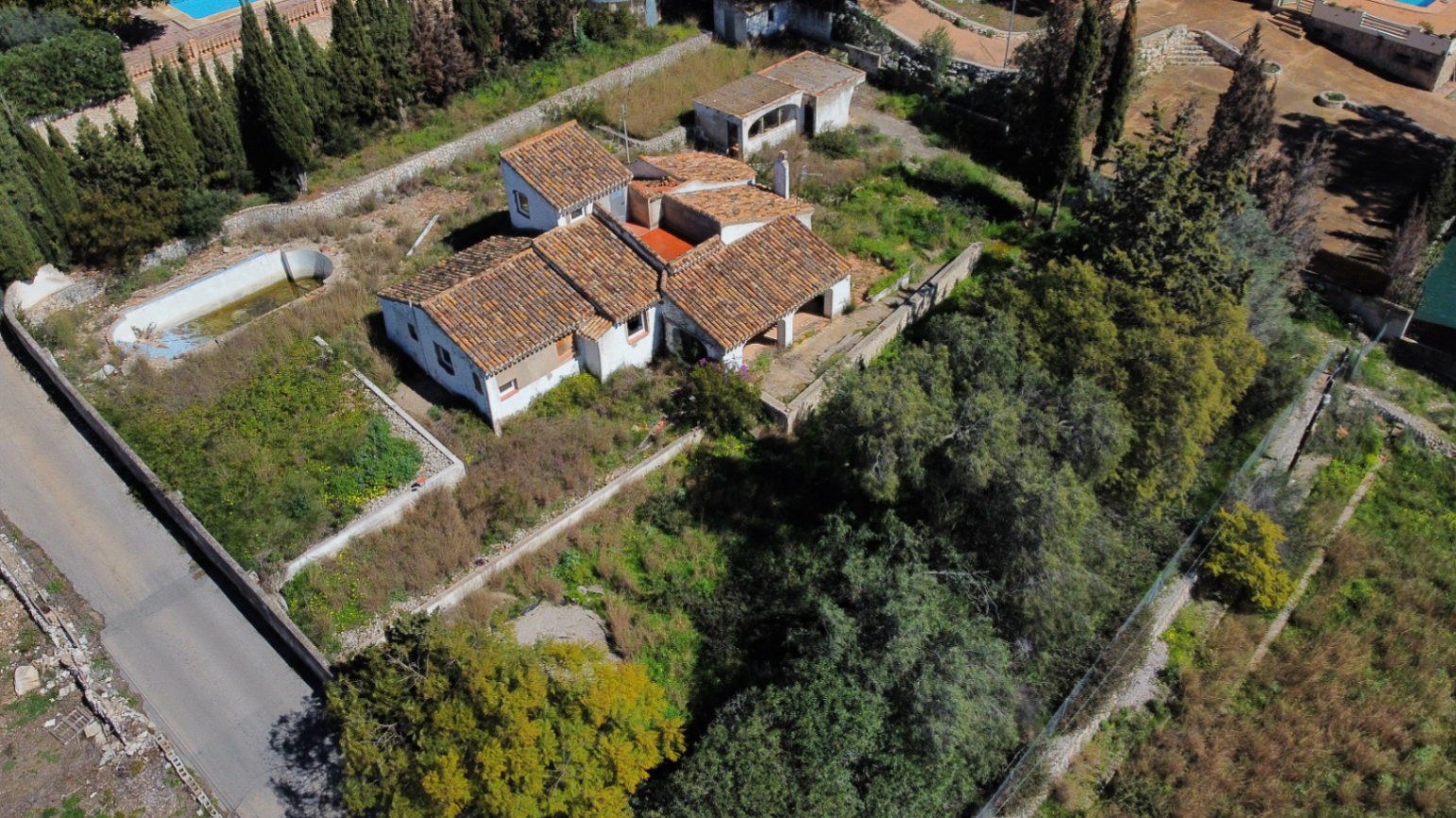 Vista aérea de la propiedad que muestra la distribución de los tejados de teja cerámica, la parcela arbolada y la piscina para reformar en la zona del Montgó.