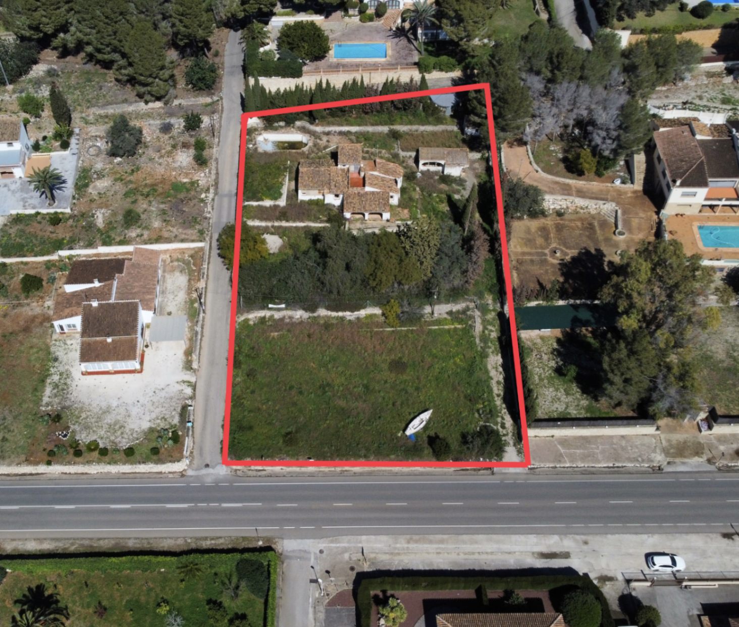 Vista aérea perimetrada de la parcela de 2.895m2 en el Montgó, mostrando la vivienda principal, construcciones anexas y el amplio terreno frontal con acceso directo desde la carretera.