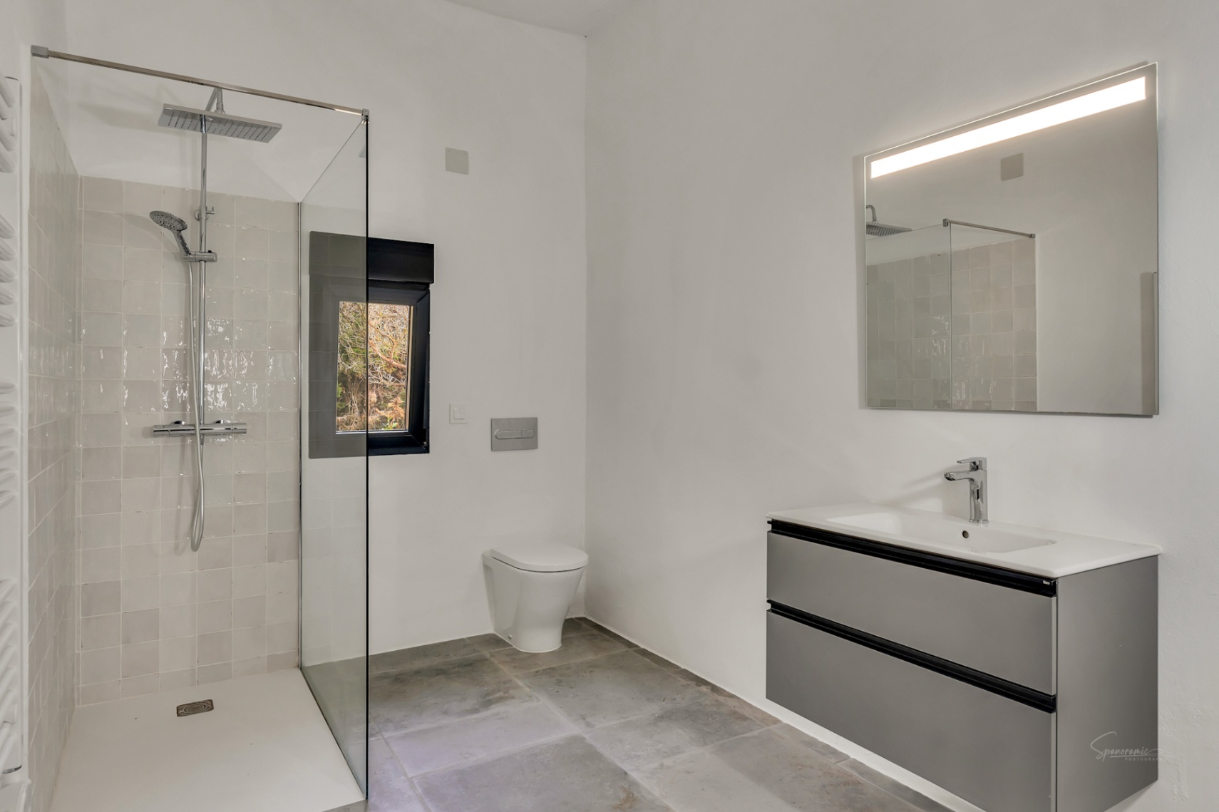 Baño moderno con ducha a ras de suelo, mampara de cristal, sanitario suspendido y mueble de lavabo flotante en gris con espejo retroiluminado.