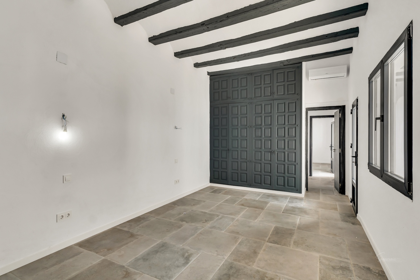 Dormitorio con vigas de madera oscura, suelos de piedra natural y un amplio armario empotrado de diseño clásico en tono gris antracita.