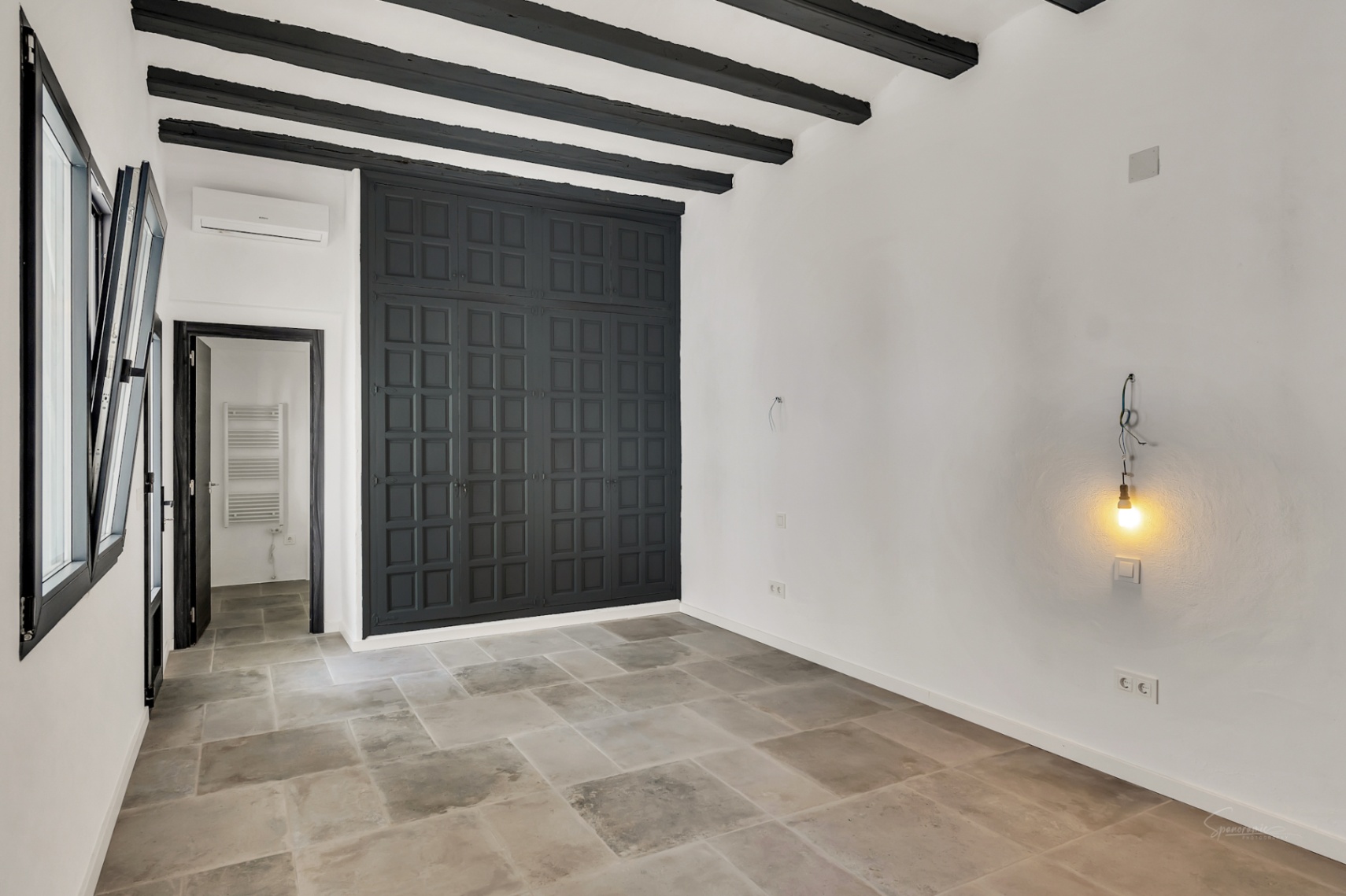 Dormitorio con vigas de madera oscura, suelos de piedra natural y un gran armario empotrado de paneles negros. Incluye aire acondicionado y acceso a zona de baño.