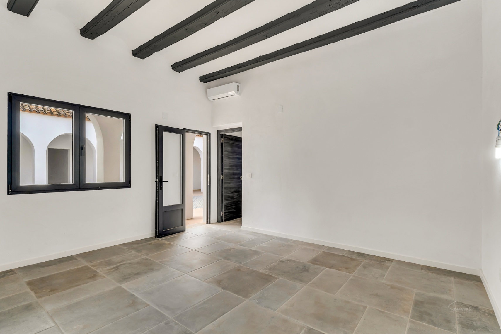 Habitación con vigas de madera oscura, suelos de piedra natural y vistas directas al patio interior de arcos tradicionales.