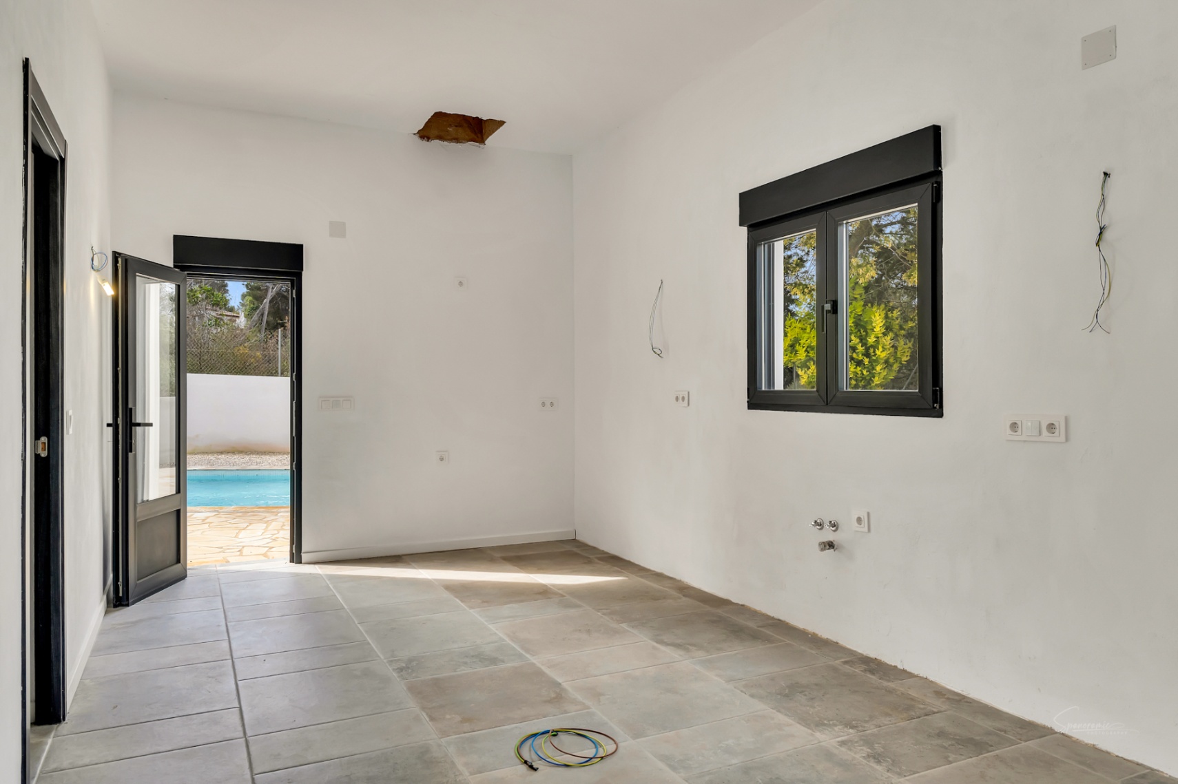 Habitación en proceso de reforma con suelos de gres porcelánico, carpintería negra y acceso directo a la terraza con piscina.