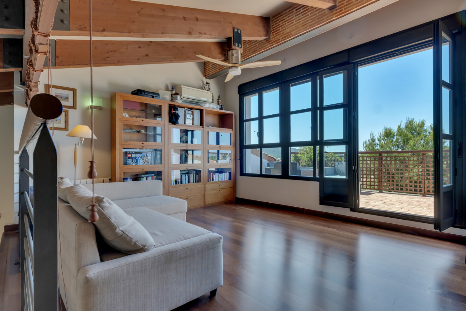 Dormitorio u oficina en planta superior con techos de vigas de madera, suelos de parqué y acceso directo a una terraza privada con vistas despejadas.