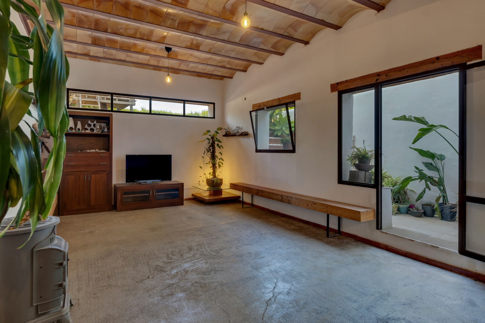 Sala de estar en planta inferior con techos de bovedilla cerámica, estufa de leña y acceso directo a un patio interior luminoso con plantas ornamentales.