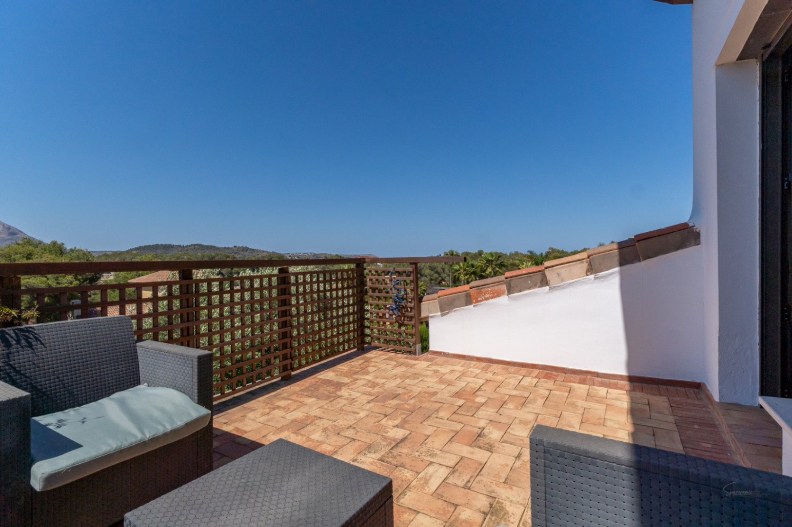 Terraza privada en la planta superior con suelo de barro cocido, mobiliario de mimbre sintético y vistas despejadas al entorno natural de Jávea.