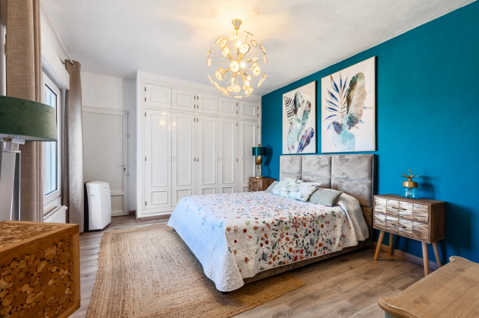 Dormitorio con pared de acento en azul turquesa, armarios empotrados blancos, suelos de madera y una lámpara de diseño dorado que aporta calidez al espacio.
