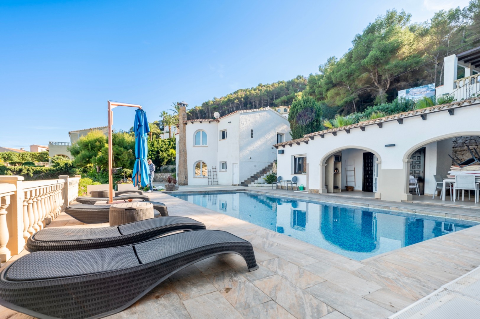 Terraza exterior con piscina rectangular, tumbonas ergonómicas y porche de arcos tradicionales frente a la fachada blanca de la villa en Portitxol.