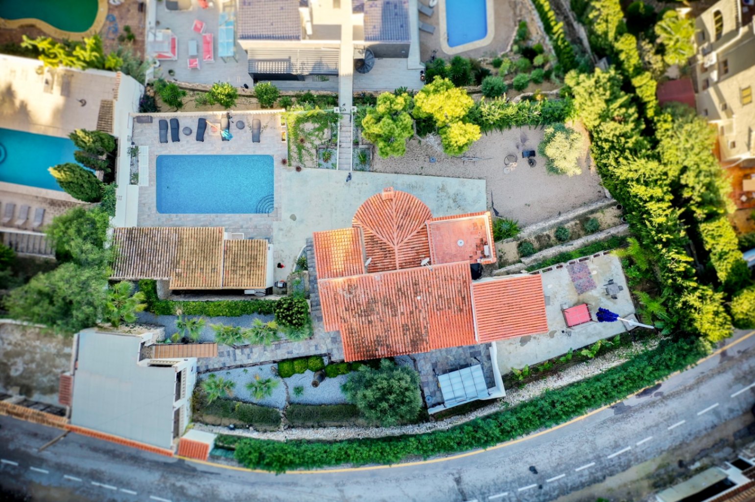 Vista aérea cenital de la villa que muestra el tejado de teja roja, la piscina rectangular con solárium y la distribución de la parcela ajardinada en Portitxol.