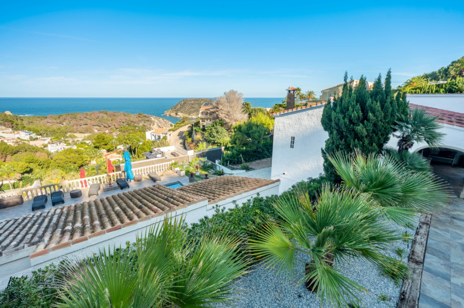 Vista panorámica desde la propiedad hacia el mar Mediterráneo, destacando los tejados de teja tradicional y el jardín con vegetación autóctona.