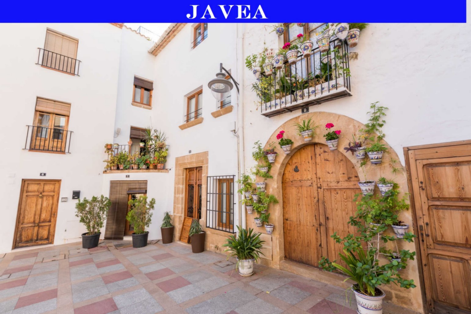 Fachada tradicional en Jávea con puertas de madera, arcos de piedra tosca y balcones decorados con macetas de cerámica y plantas mediterráneas.