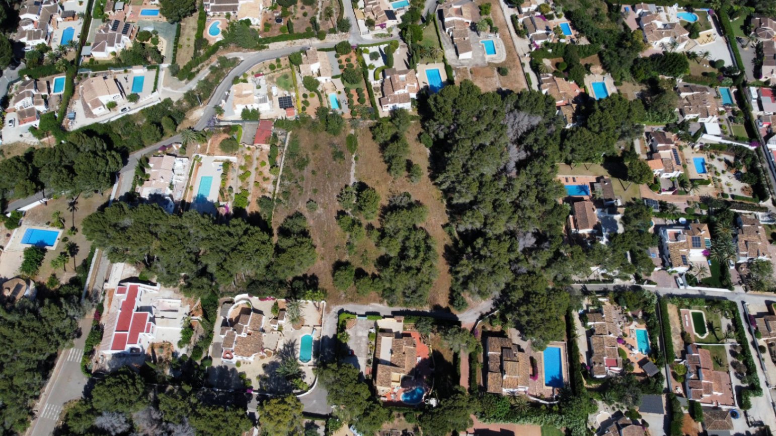 Vista aérea de la amplia parcela llana rodeada de villas residenciales consolidadas y abundante vegetación mediterránea en Jávea.